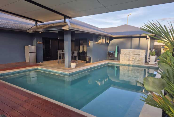 Pool with timber decking and a stone feature wall beside a covered patio